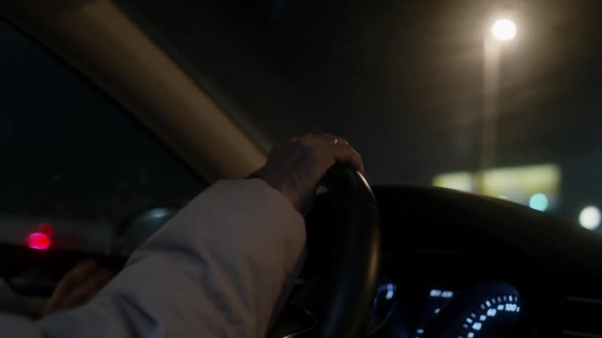 Female driver drives car past brightly lit buildings at night