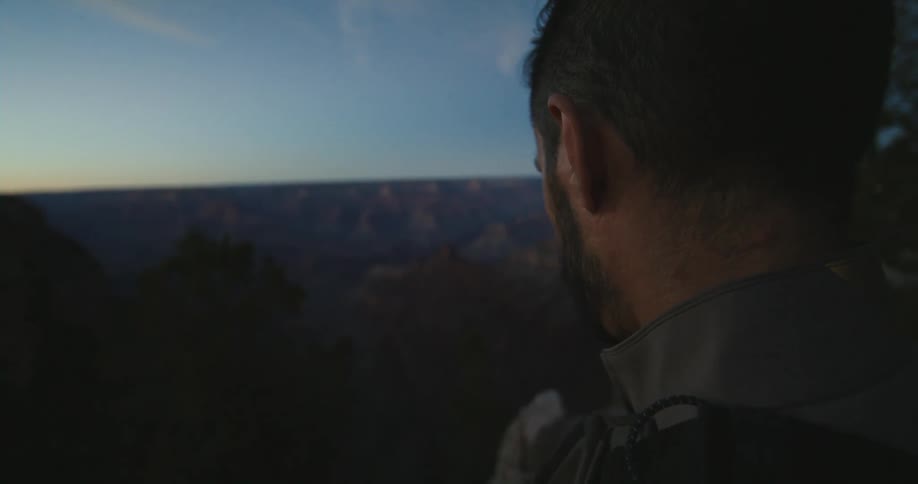 Man is looking down a canyon while observing the sunset