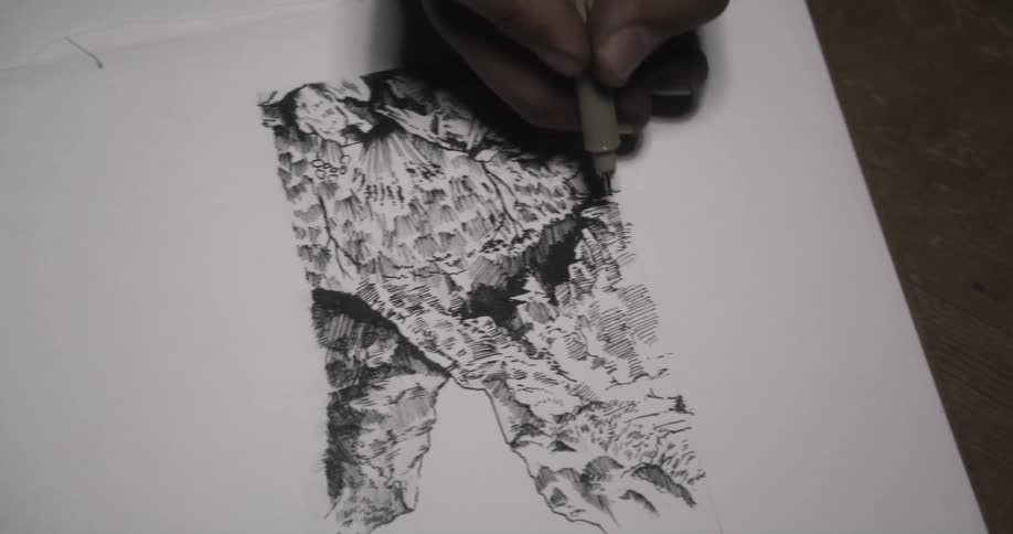 Artist draws in ink on white paper sitting on wooden surface