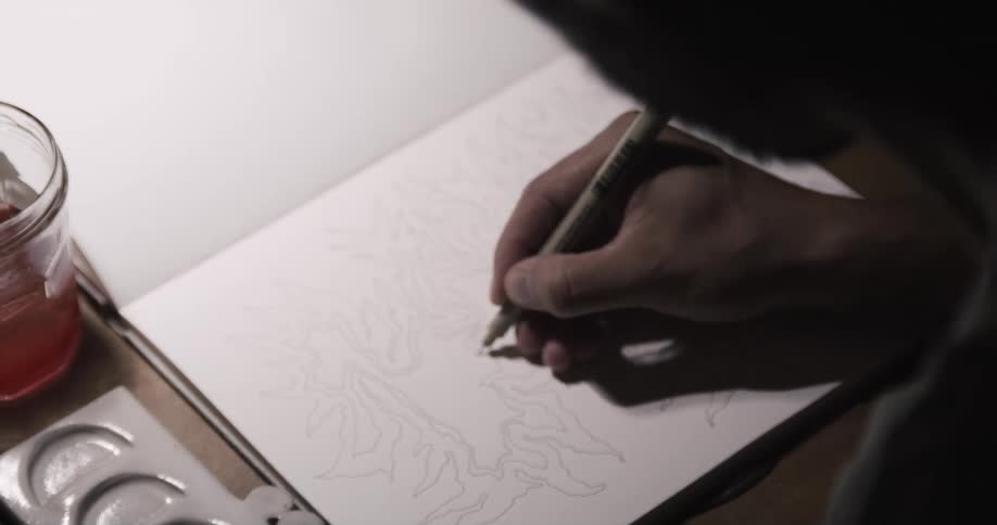 A man is sitting at a table drawing a picture with a black pen