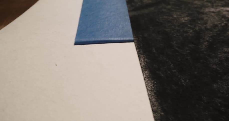 Blue painters tape is slowly peeled away from the edge of a charcoal pencil artwork