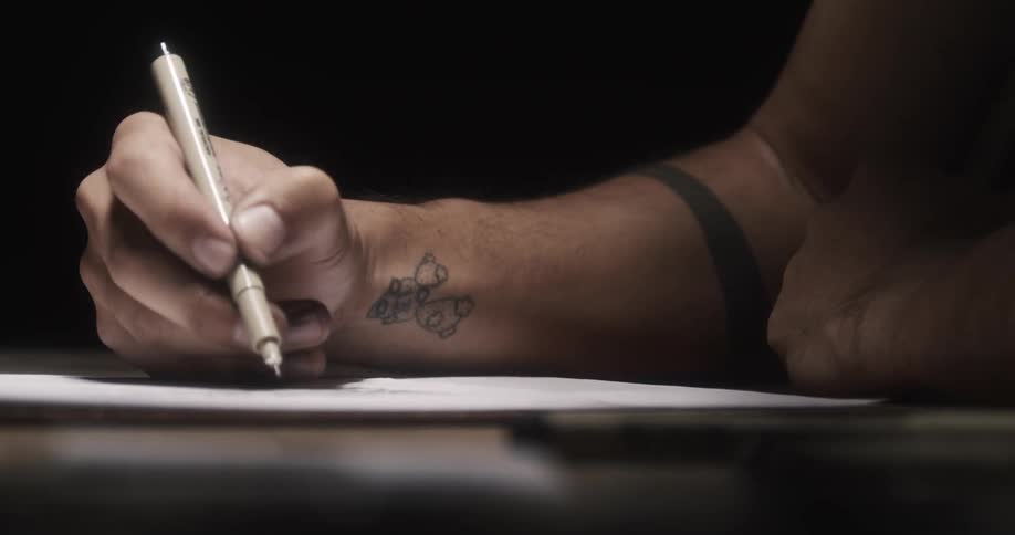 A man is sitting down at a table drawing with a black pen