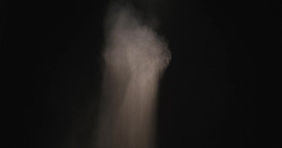 Pale powder spreads through darkness and begins to dissipate