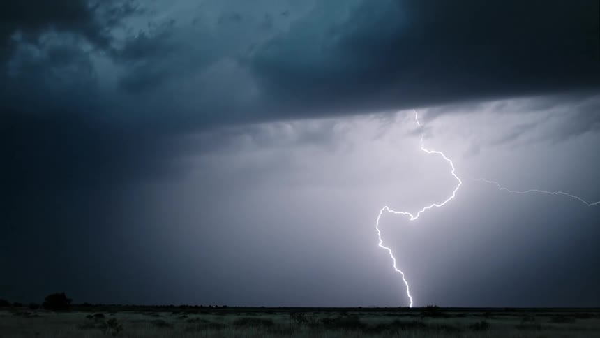 Lightning cracks across a dark sky and hits the ground flashing brightly under the clouds