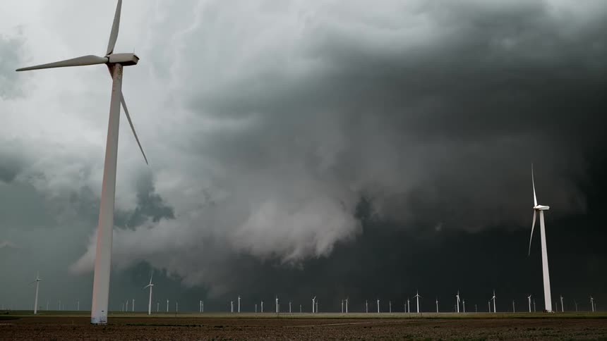 Wind turbines spin on a wind farm under a dark stormy sky