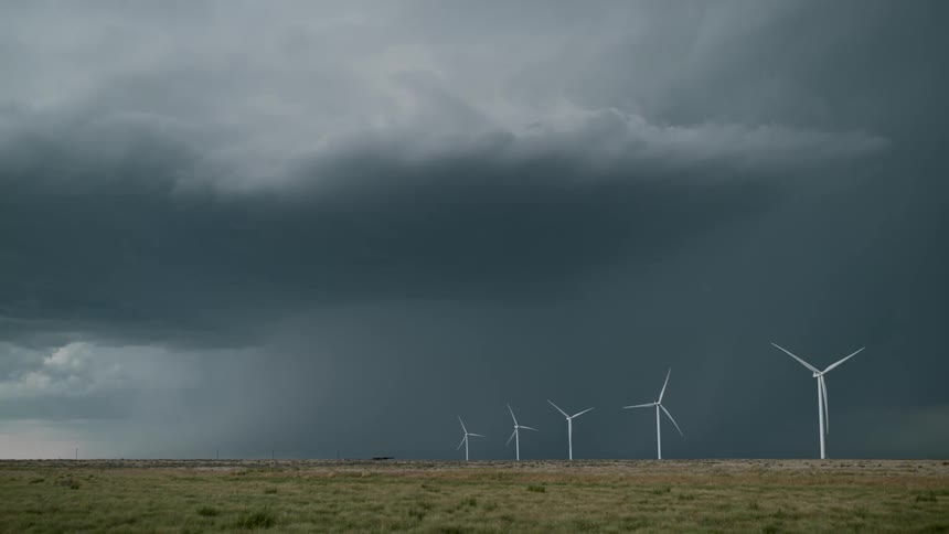 Wind turbines spin on a wind farm under a dark stormy sky