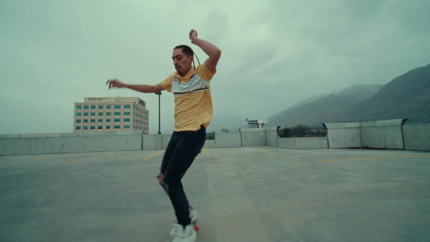 A man dances in roller skates on a rooftop in a city on a cloudy day