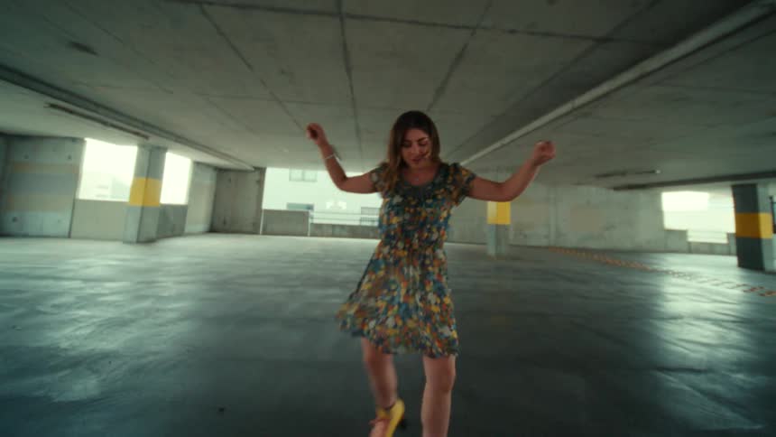 A woman wearing roller skates dances in a multilevel parking garage during the day