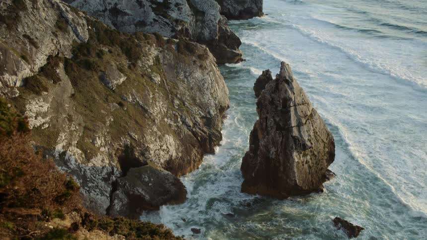 Ocean waves wash into a rocky coastline during the day
