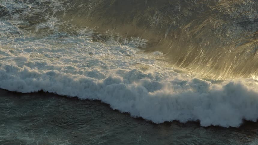 A large wave crashes in the ocean at sunset