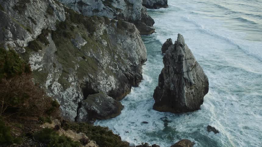 Surf crashes against moss covered cliffs and nearby outcropping