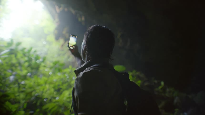 A man uses his smartphone to take photos while standing in a cave in the woods