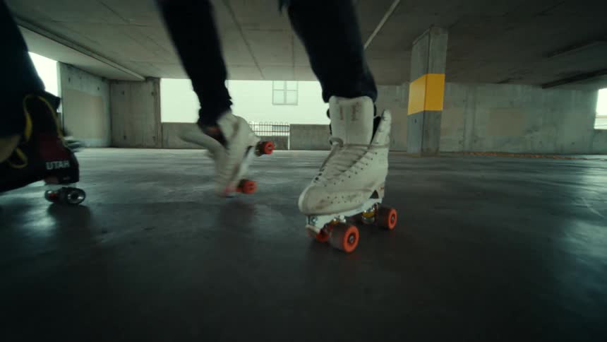A pair of men in roller skates dance side by side in a parking garage during the day