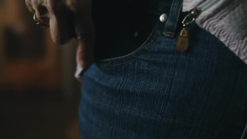A man covers his phone as he slips it into his pocket then moves his sweater to cover it