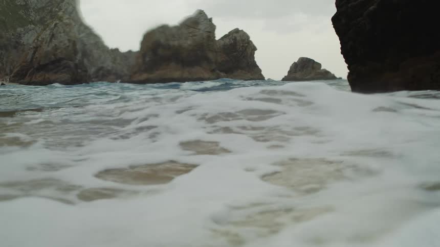 Waves crash onto beach foaming as they flow past rock outcroppings