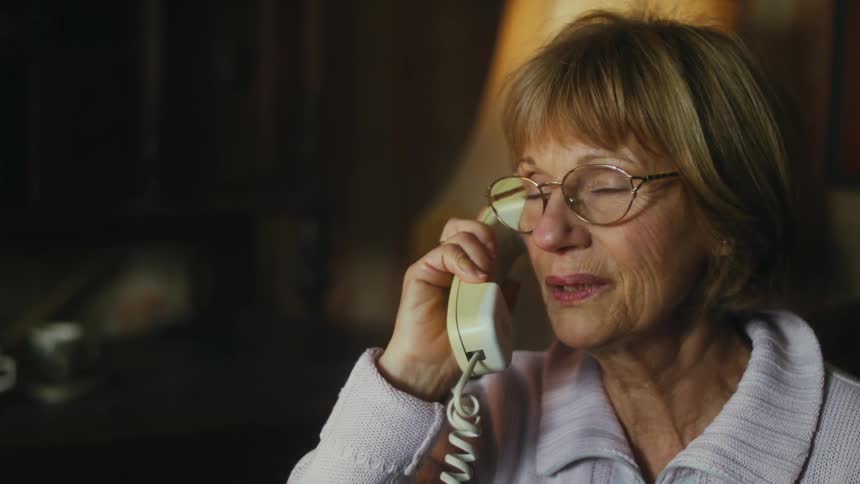 An older woman is inside a room talking on a telephone