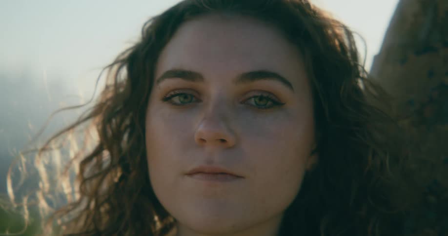 A woman leaning against a tree pushes her wind blown hair back off her face