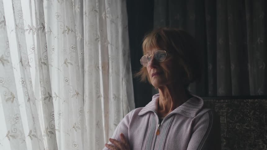 Middle aged woman stands with her arms crossed near curtained window