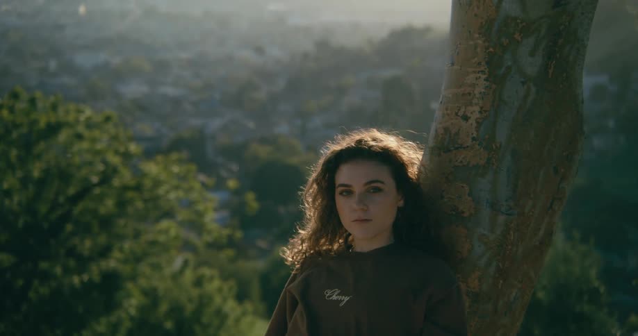Young woman leaning against a tree trunk with a skyline view behind her at a beautiful sunny day