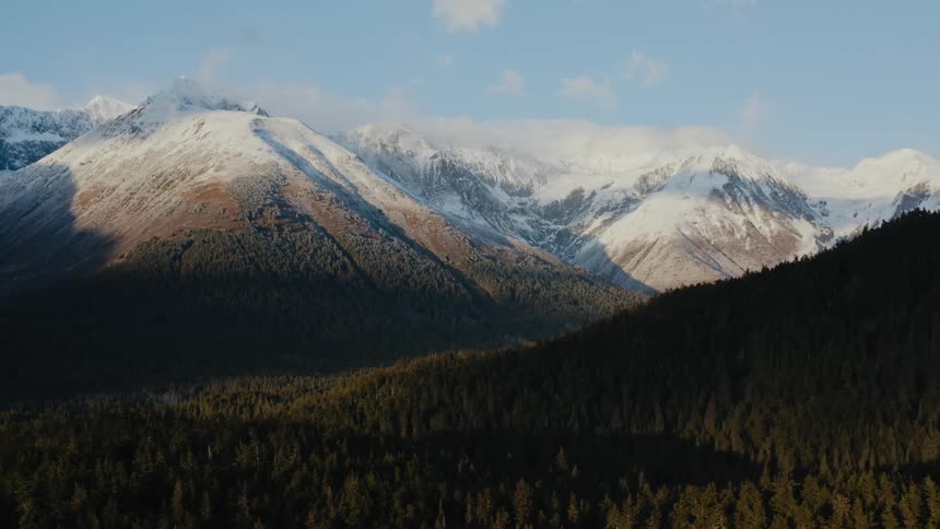 A snow capped mountain ridge across from a mountain covered in thick green forest