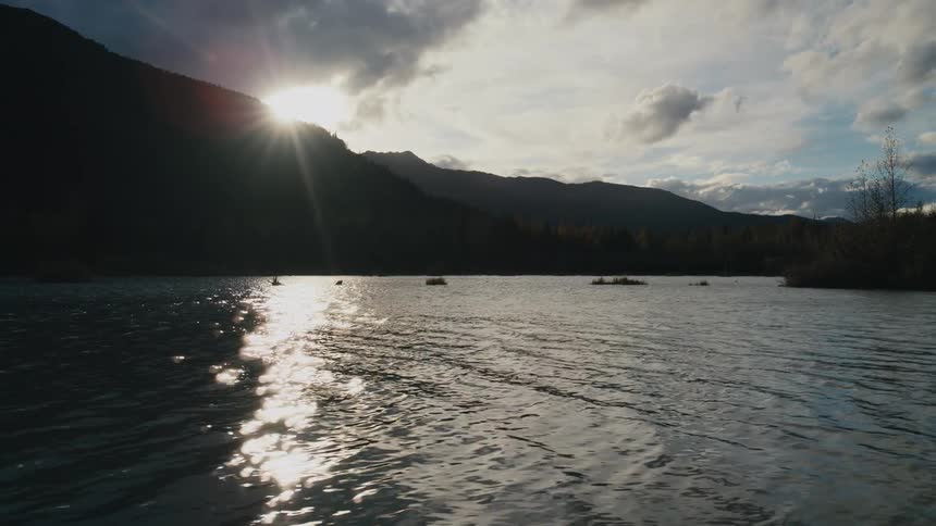 Sunlight shines over a mountain onto the surface of a lake