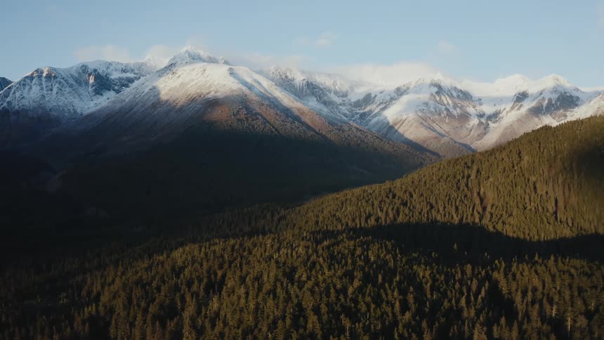 A snow capped mountain ridge looms over smaller ridge covered in dense forest