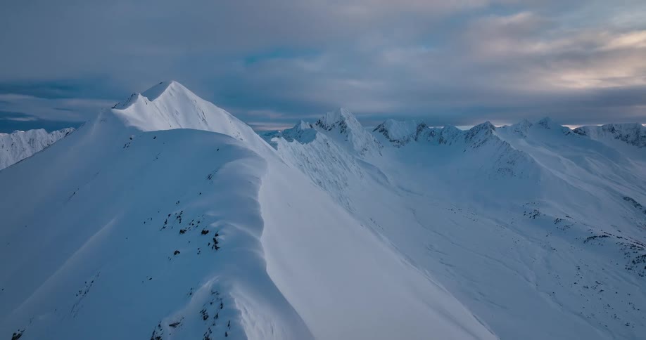 A snow covered mountain ridge with peaks high in a cloudy sky