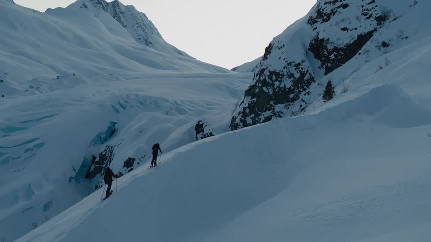 A pair of mountaineers use trekking poles as they ascend a snow covered mountain slope during the day