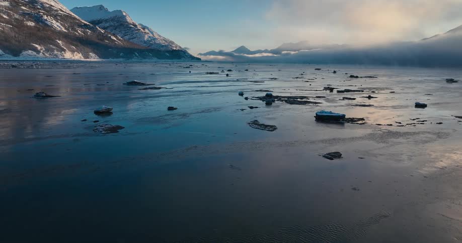 Ice floats on reflective water with snow covered mountains in the background