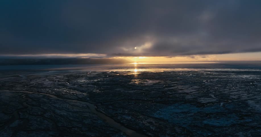 Bright sun shines from near horizon onto frozen area under an overcast sky