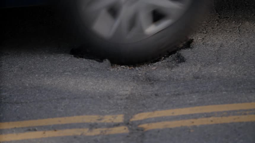 An automobile drives over a hole in the road