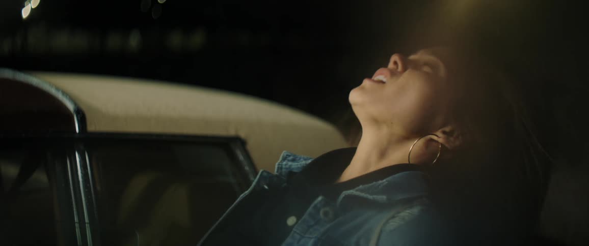 A woman standing next to an older car suddenly throws her head back as flashes go off