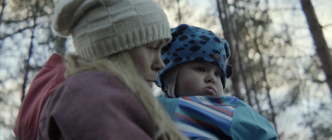 A woman holding a toddler outdoors during the day is talking to the toddler