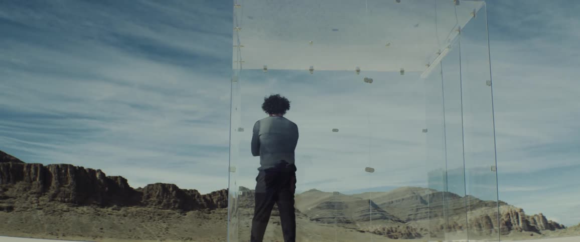 A man paces inside a clear box in a canyon
