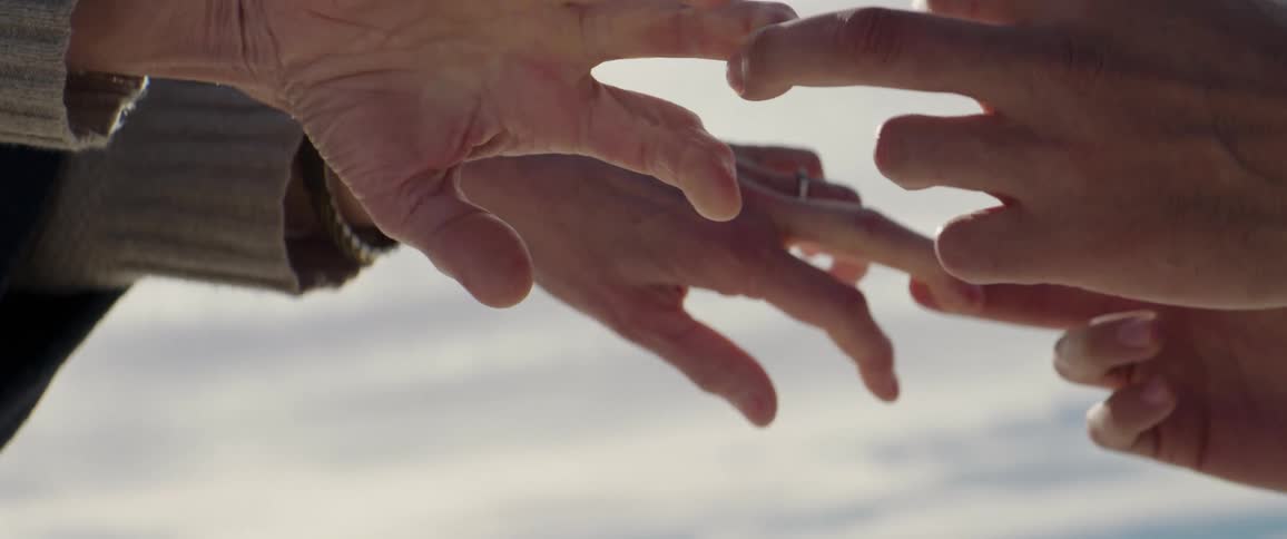 Man and woman hold both each others hands then let go while standing outdoors under cloudy sky