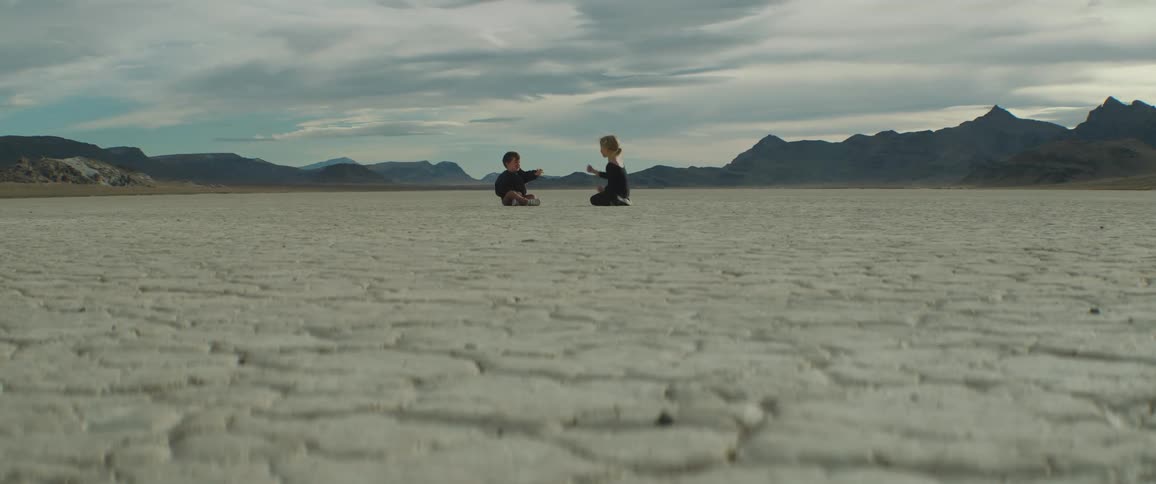 Boy and girl talk while sitting on arid desert ground between mountains