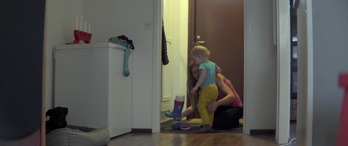 A woman is helping a child get dressed, but he walks away
