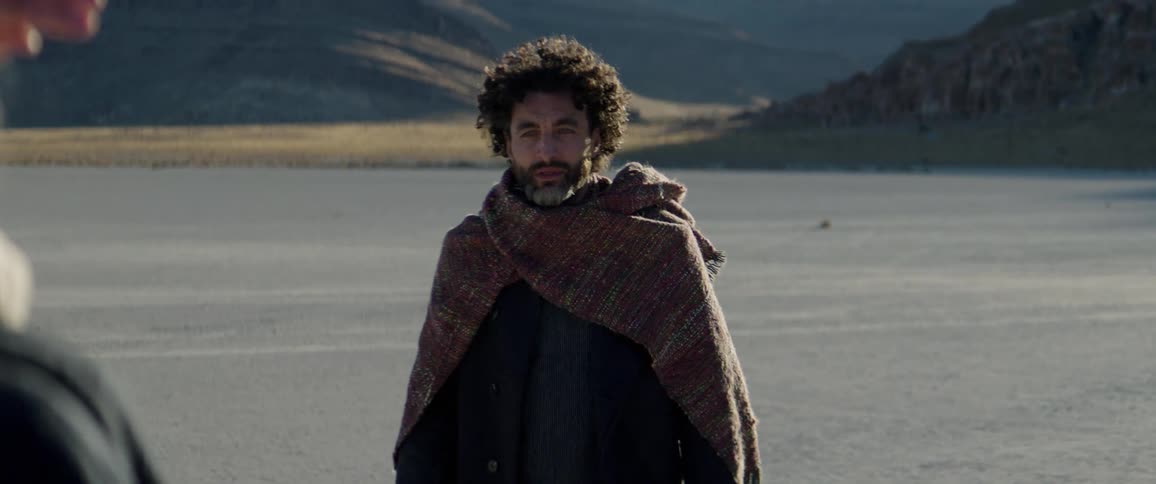 A man and woman in a desert walk towards one another and then circle as they look at one another