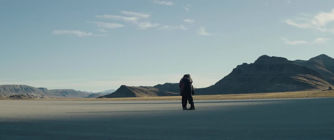 A man and woman in a desert hug one another
