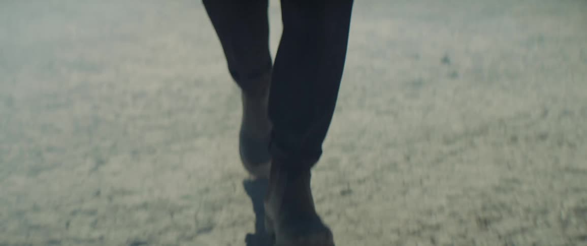 Man walks across arid ground as smoke flows between him and the mountains behind him