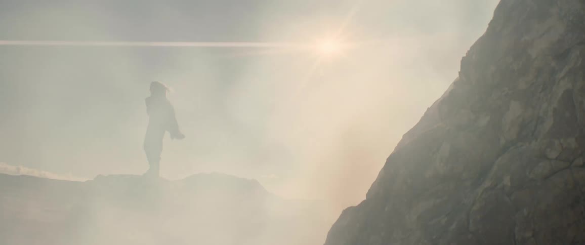Person stands on outcropping overlooking landscape on foggy day under a bright sun