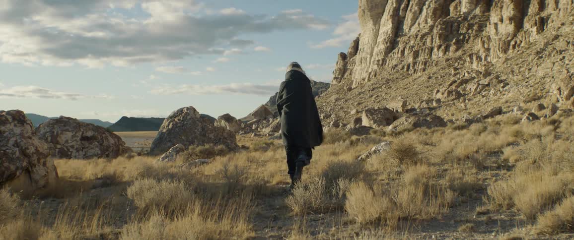 A woman slowly walks through a rocky field in badlands during the day