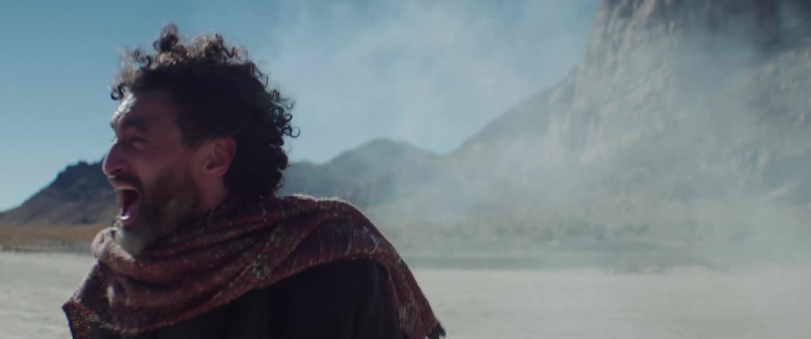 A man yells as he turns around walking near mountains