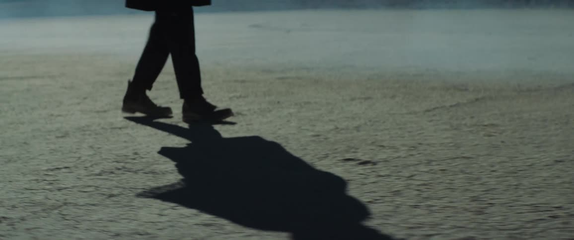 A man in boots is walking backwards in the foggy desert