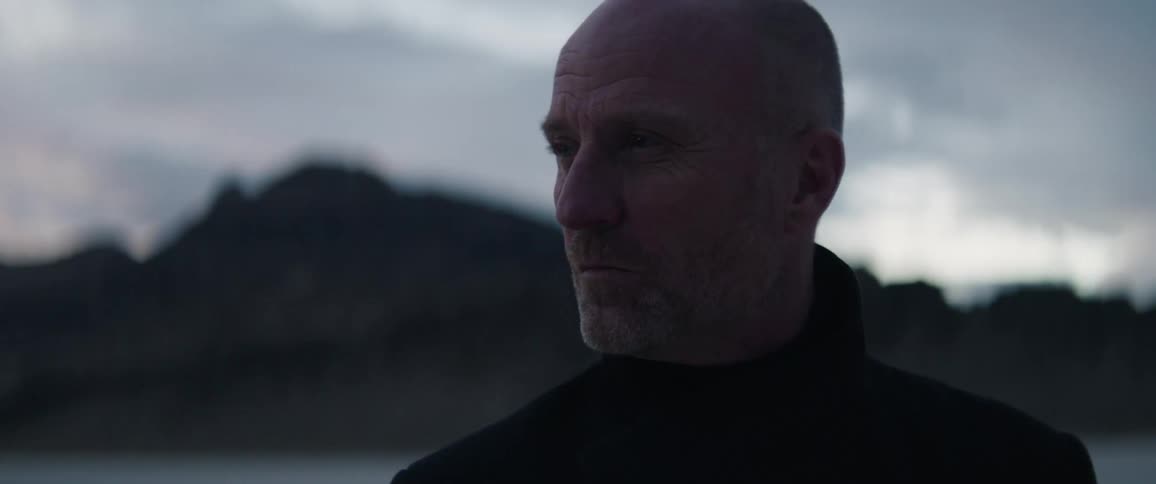 Bald man with black turtleneck sweater turns around in the field at dusk