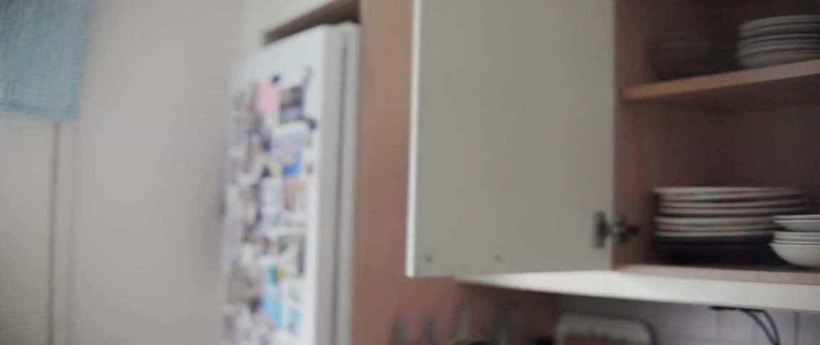 Young woman stacking plates inside a kitchen cupboard while tidying her modern home interior.
