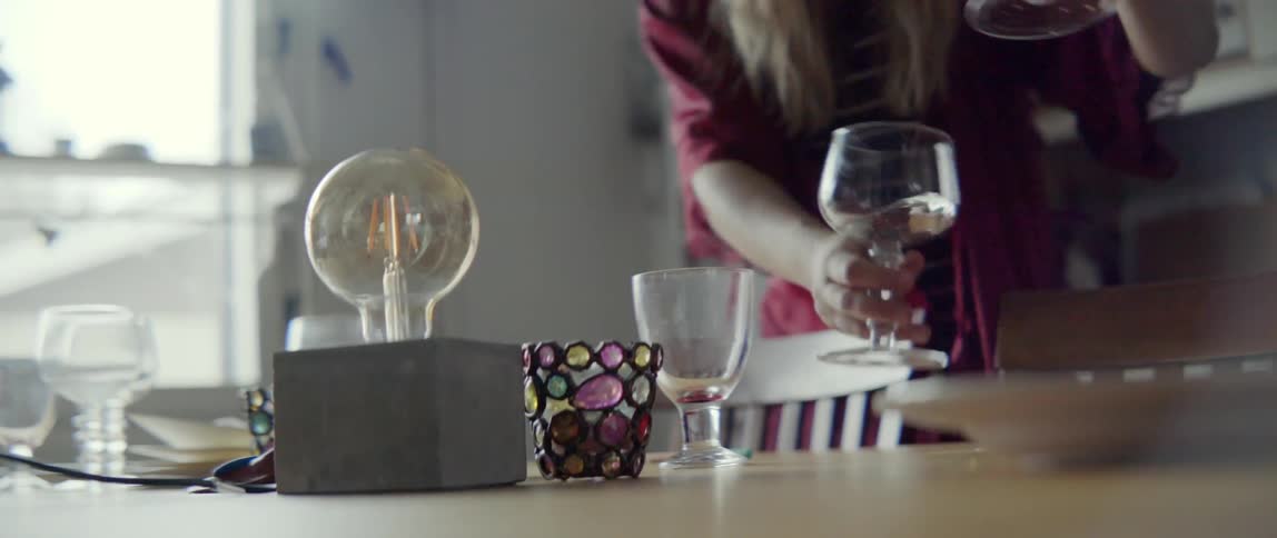 A woman moves dirty glasses from a dining table to another area in a kitchen