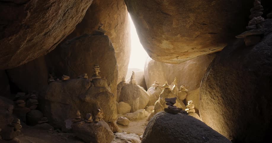 Sunlight shines through an opening into a cave filled with boulders and stacks of stones