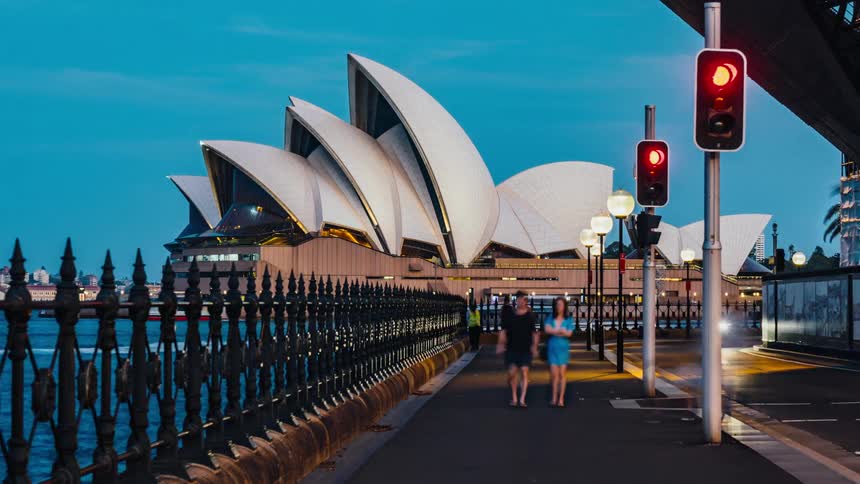 People drive and walk by the Sydney opera house on the water