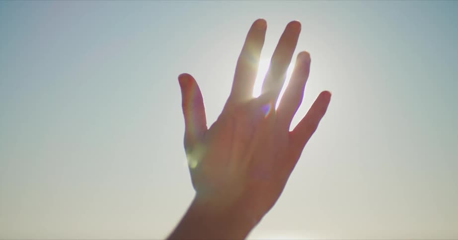 A person is holding their hand up and the sun is shining behind it